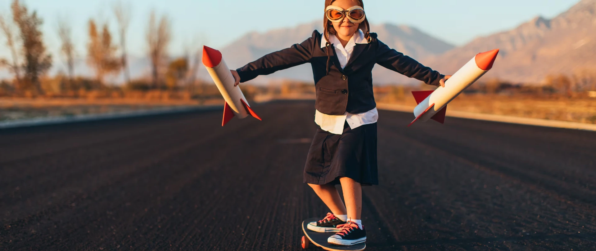Kind mit Fliegerbrille und Raketen auf einem Skateboard