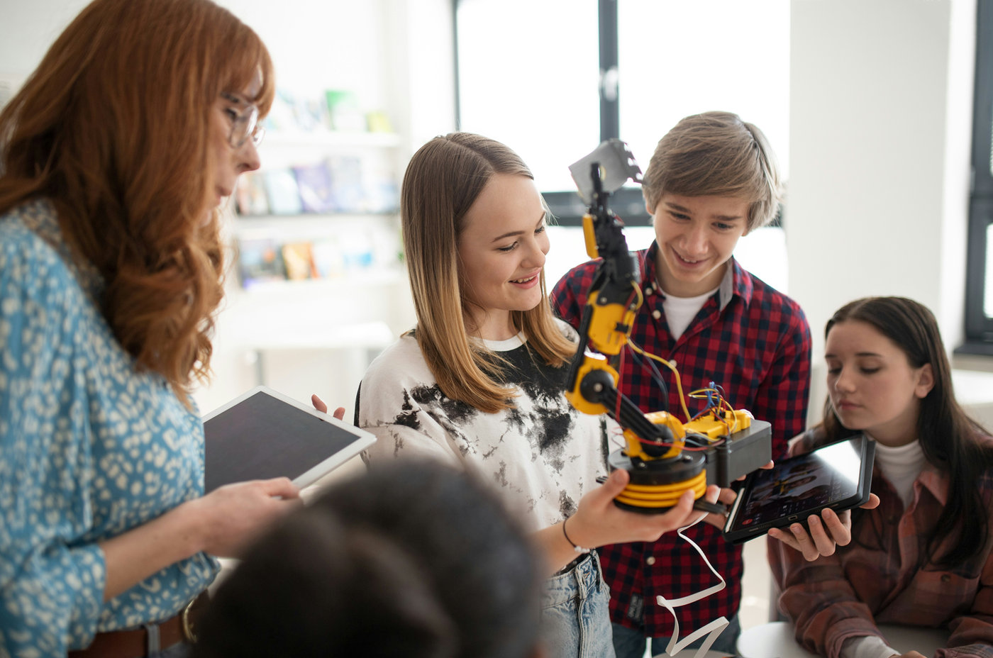 Lehrerin und Jugendliche arbeiten mit einem Roboterarm